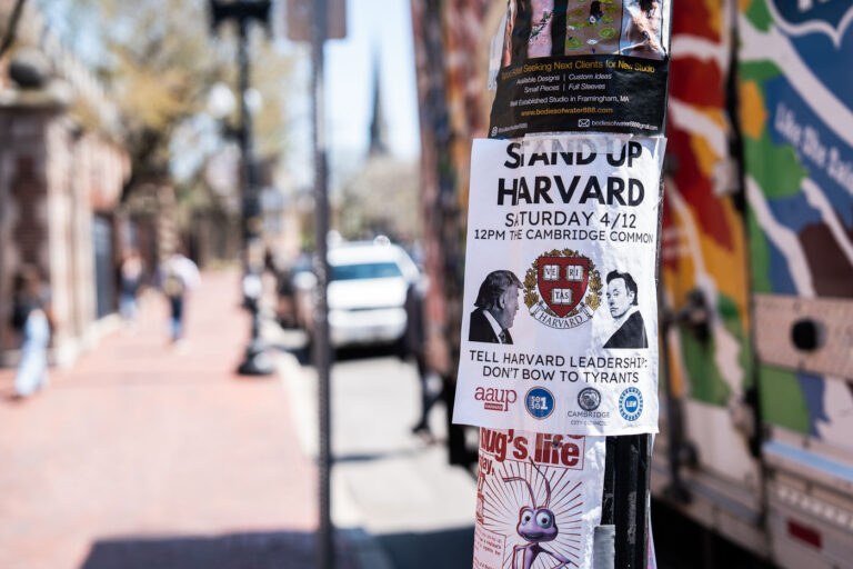 Protest Flyer Near Harvard Square, Cambridge 1 A politically charged flyer near Harvard Square calls for a demonstration at the Cambridge Common, urging the university community to “Stand Up Harvard.” Affixed to a utility pole along Massachusetts Avenue, it features the Harvard crest and contrasting portraits of public figures, symbolizing tension between authority and academic independence. The red-brick sidewalks and blurred foot traffic behind it evoke the constant movement and civic engagement that define this historic Cambridge neighborhood.