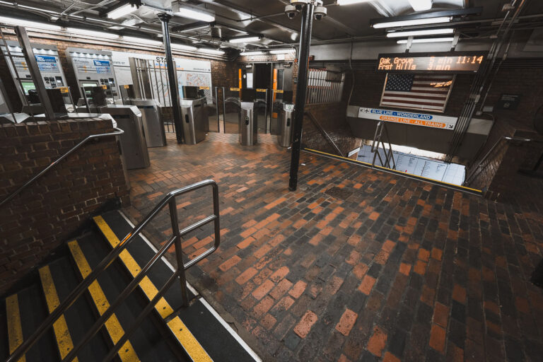 State Street Station Fare Control, Boston 2 The entrance and fare control area at State Street Station, a key interchange in downtown Boston where the Orange Line and Blue Line intersect. The station opened in 1908 as part of the Washington Street Tunnel and remains one of the MBTA’s oldest continuously operating rapid transit facilities. Brick flooring, steel columns, and low ceilings reflect early 20th-century subway construction, while modern fare gates and electronic arrival boards show later upgrades layered onto the original structure. The signage directing riders to Oak Grove, Forest Hills, and Wonderland highlights the station’s role as a transfer point connecting North Shore riders, downtown commuters, and the broader MBTA network.