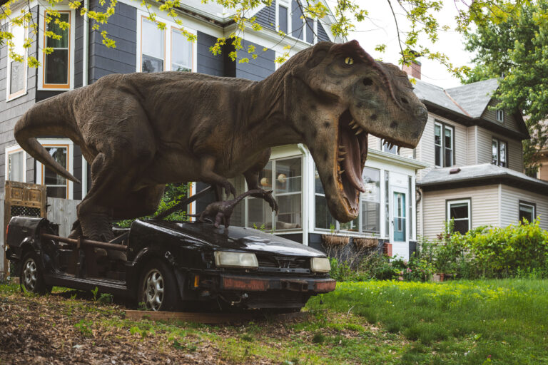 T. rex yard display in South Minneapolis 3 T. rex yard display with a smaller dinosaur figure in South Minneapolis.