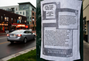 A flyer urging people to call Minnesota Governor Tim Walz and demand he veto HF1, a bill repealing MinnesotaCare coverage for undocumented adults. The flyer has bold text reading “CALL WALZ TO TELL HIM: VETO HF1! PROTECT HEALTHCARE FOR IMMIGRANTS!” It states that the Minnesota House and Senate passed the bill and criticizes lawmakers for supporting it. The flyer provides a sample script for callers, emphasizing that denying healthcare to immigrants is inhumane and harmful to all residents. At the bottom, it lists the governor’s phone number: 651-201-3400, and includes the logo of MIRAC (Minnesota Immigrant Rights Action Committee).