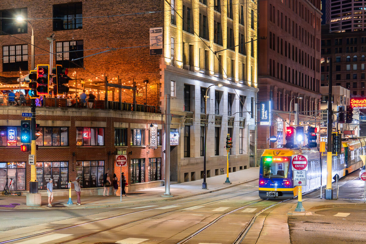 Light rail train goes in front of a bar with people on roof at night