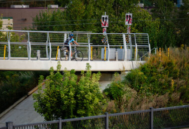A cyclist travels across the Martin Olav Sabo Bridge, a dedicated pedestrian and bicycle suspension bridge spanning Hiawatha Avenue in Minneapolis. Opened in 2007, the bridge was designed to provide a safe, grade-separated connection for trail users along the Midtown Greenway, avoiding the busy highway and light-rail tracks below. The bridge reflects Minneapolis’ investment in protected urban cycling infrastructure, supporting its reputation as one of the most bike-friendly cities in the United States.