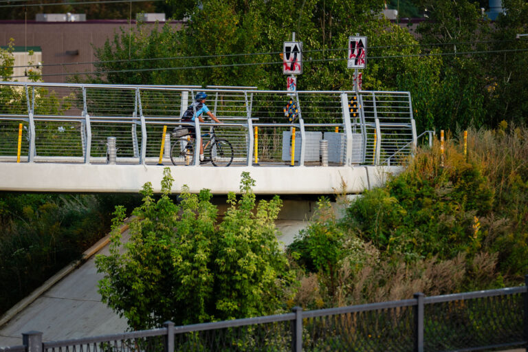 Martin Olav Sabo Bridge Cyclist Crossing 1 A cyclist travels across the Martin Olav Sabo Bridge, a dedicated pedestrian and bicycle suspension bridge spanning Hiawatha Avenue in Minneapolis. Opened in 2007, the bridge was designed to provide a safe, grade-separated connection for trail users along the Midtown Greenway, avoiding the busy highway and light-rail tracks below. The bridge reflects Minneapolis’ investment in protected urban cycling infrastructure, supporting its reputation as one of the most bike-friendly cities in the United States.