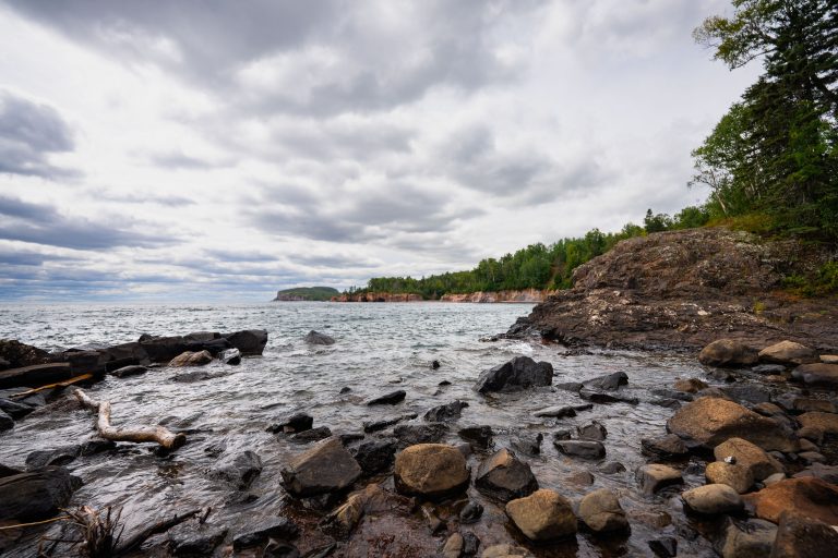 Rocky shoreline of Lake Superior at Tettegouche State Park with forested cliffs in the distance.