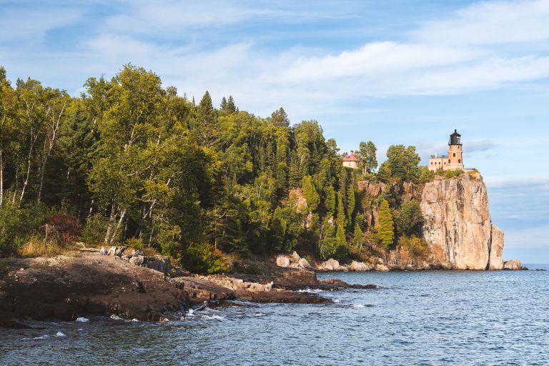 Split Rock Lighthouse stands on a cliff above Lake Superior's rocky shoreline surrounded by forest.
