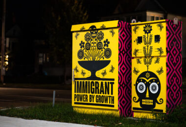 Electrical boxes with artwork on them reading: "Immigrant Power By Growth".