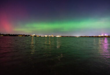Downtown Minneapolis seen below the Northern Lights at Bde Maka Ska.