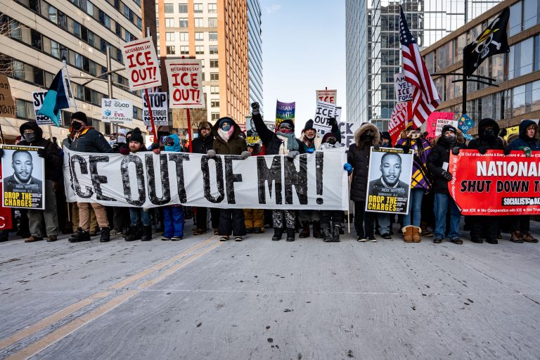 Minneapolis Protest Against ICE Deployment 4 Protesters march in downtown Minneapolis holding signs and banners against ICE deployment.