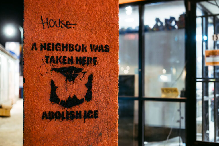 Abolish ICE Graffiti, Bloomington Ave, Minneapolis 2 Graffiti reading "A neighbor was taken here" and "Abolish ICE" is spray-painted on a textured orange pillar at the intersection of Lake Street and Bloomington Avenue in Minneapolis. The message refers to the Immigration and Customs Enforcement (ICE) agency and likely relates to protests against immigration policies and enforcement actions. The phrase "A neighbor was taken here" suggests a personal experience or observation of an individual being detained or deported, highlighting community impact and opposition to ICE's presence and operations. This form of street art serves as a public statement and a form of protest within the urban environment.