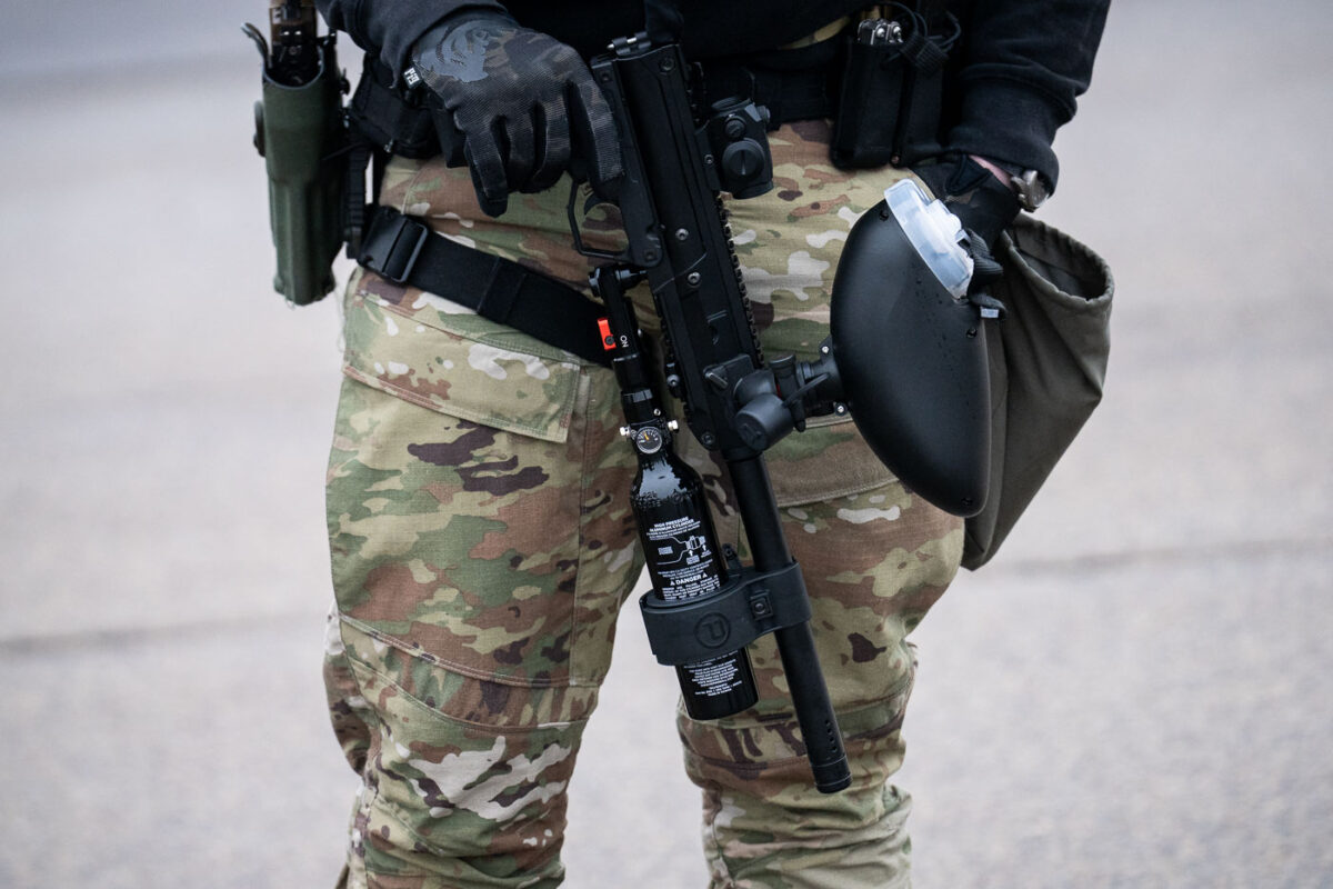 A Border Patrol officer stands outside the Whipple building near Minneapolis with a less lethal weapon.