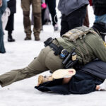 Border Patrol Officer pushes woman to the ground, Minneapolis 1 A protester is arrested outside the Whipple Federal Building outside Minneapolis.Protests have gathered outside the fenced in building as hundreds of agents stand outside the fence.