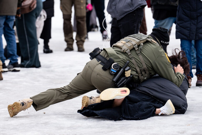 Border Patrol Officer pushes woman to the ground, Minneapolis 2 A protester is arrested outside the Whipple Federal Building outside Minneapolis.Protests have gathered outside the fenced in building as hundreds of agents stand outside the fence.