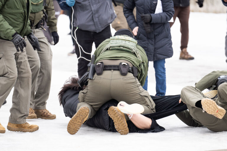 Border Patrol officers and protester in Minneapolis 3 A protester is arrested outside the Whipple Federal Building outside Minneapolis.Protests have gathered outside the fenced in building as hundreds of agents stand outside the fence.