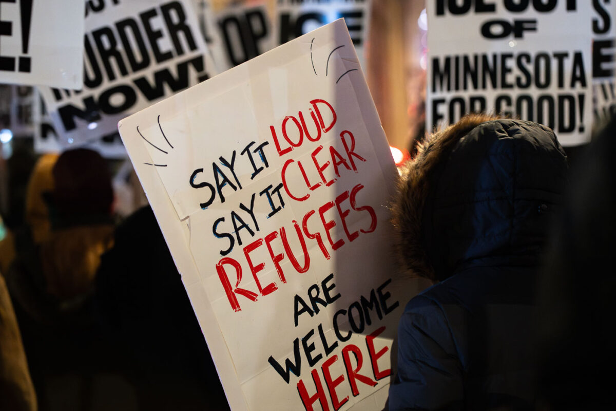 Protesters holding up signs at a "Bye Bye Bovino" protest in downtown Minneapolis. Protester holding up a sign "Say It Loud Say It Clear Refugees Are Welcome Here"