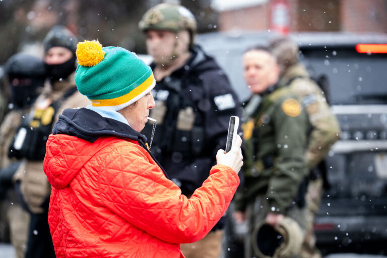 Greg Bovino watches observer blowing whistle 1 An observer blows a whistle at a gas station as Border Patrol commander Gregory Bovino looks on.