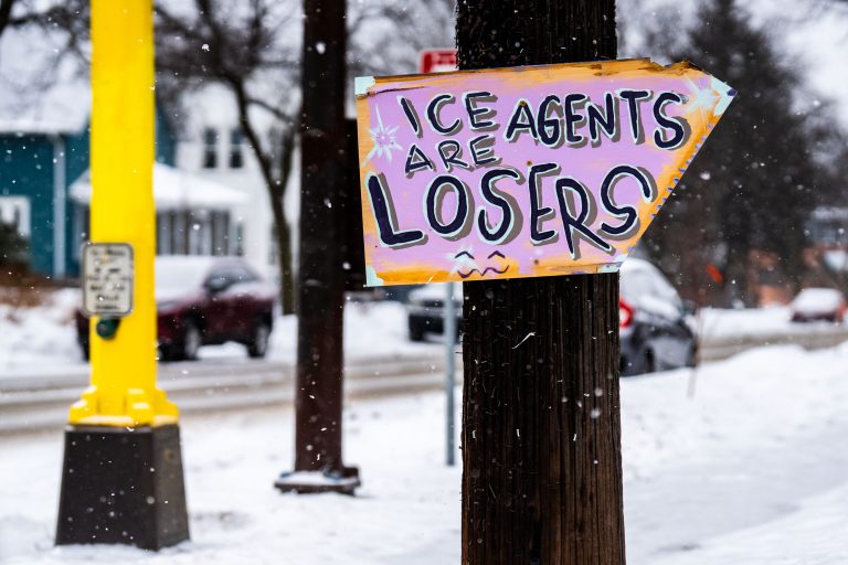 Minneapolis Protest Sign: ICE Agents Are Losers 1 A handmade protest sign reading "ICE AGENTS ARE LOSERS" is displayed on a wooden pole in Minneapolis during a snowstorm.