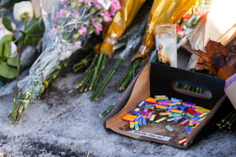 Whistles for ICE Warning at Renee Good Memorial, Minneapolis 3 Colorful whistles in a cardboard tray beside flowers and a memorial candle at the Renee Good Memorial in Minneapolis.