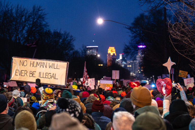 Minneapolis Vigil for Renee Good: Protest Against ICE 4 Protesters in South Minneapolis hold signs opposing ICE and immigration policies, with the city skyline in the background.