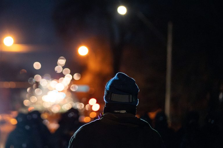 Minneapolis: Federal Officer Shoots Man Amidst ICE Operation 2 A person wearing a blue beanie stands in front of blurred lights during an ICE operation in Minneapolis.