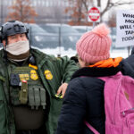 Protester with sign and Border Patrol agent in Minneapolis 4 A protester holds up a sign that reads "Whose mom will you take today?" in front of a Border Patrol Federal Agent.