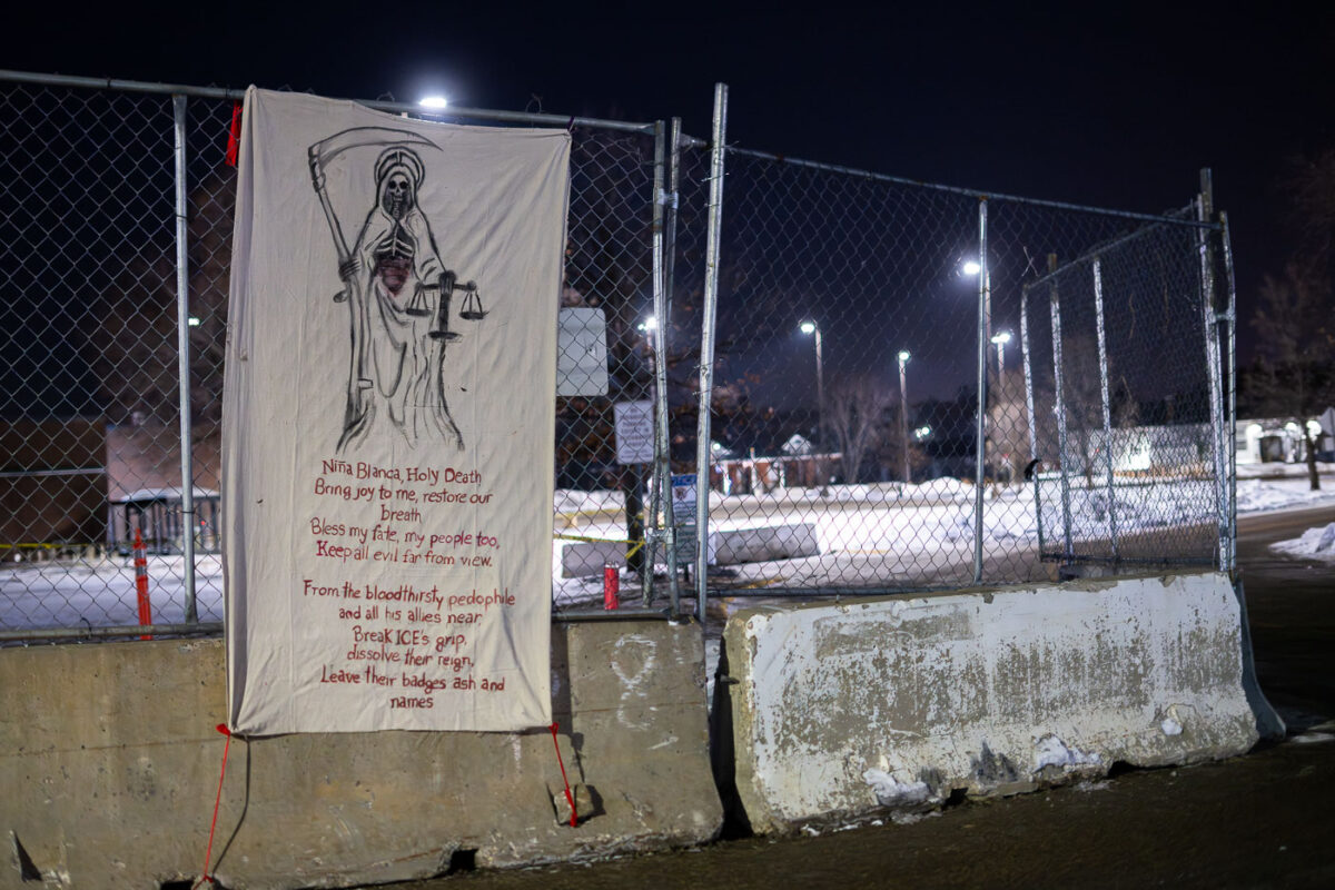 A banner on the fencing around the Whipple federal building in Minneapolis. The building is used as a ICE detention center and base during current operations in Minnesota. “Nina Blanca Holy DeathBring joy to me, restore our breathBless my fate, my people too,Keep all evil far from view.From the bloodthirsty pedophileand all his allies nearBreak ICE’s grip,dissolve their reign,Leave their badges ash and names”