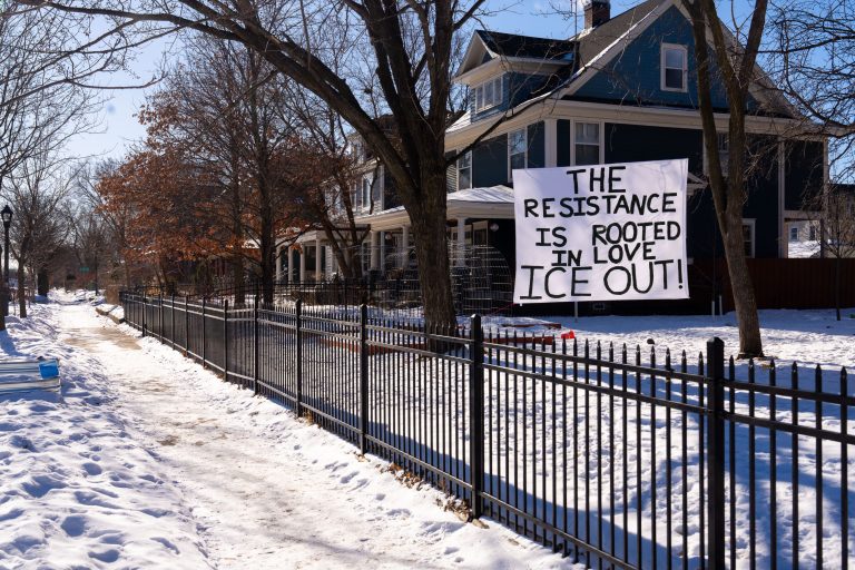 South Minneapolis "ICE OUT" Protest Banner 2 A protest banner reading "The resistance is rooted in love ICE OUT!" hangs between trees in South Minneapolis.