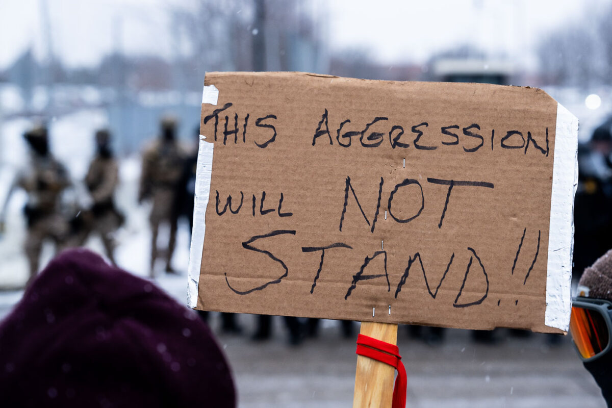 Protester at the Whipple building in Minneapolis on January 17, 2026 holding a protest sign that reads "This aggression will not stand".