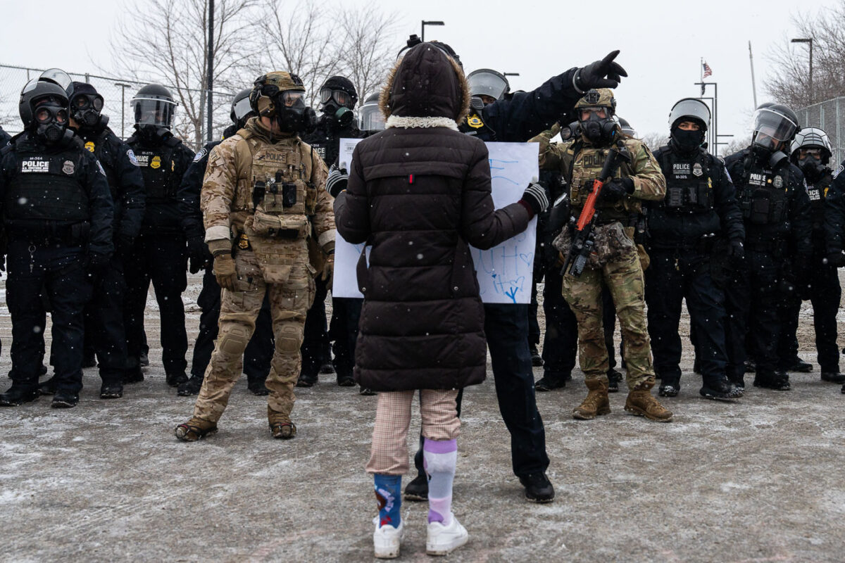Protester holds up a sign in front of Border Patrol BORTAC officers in Minneapolis on January 16, 2026.