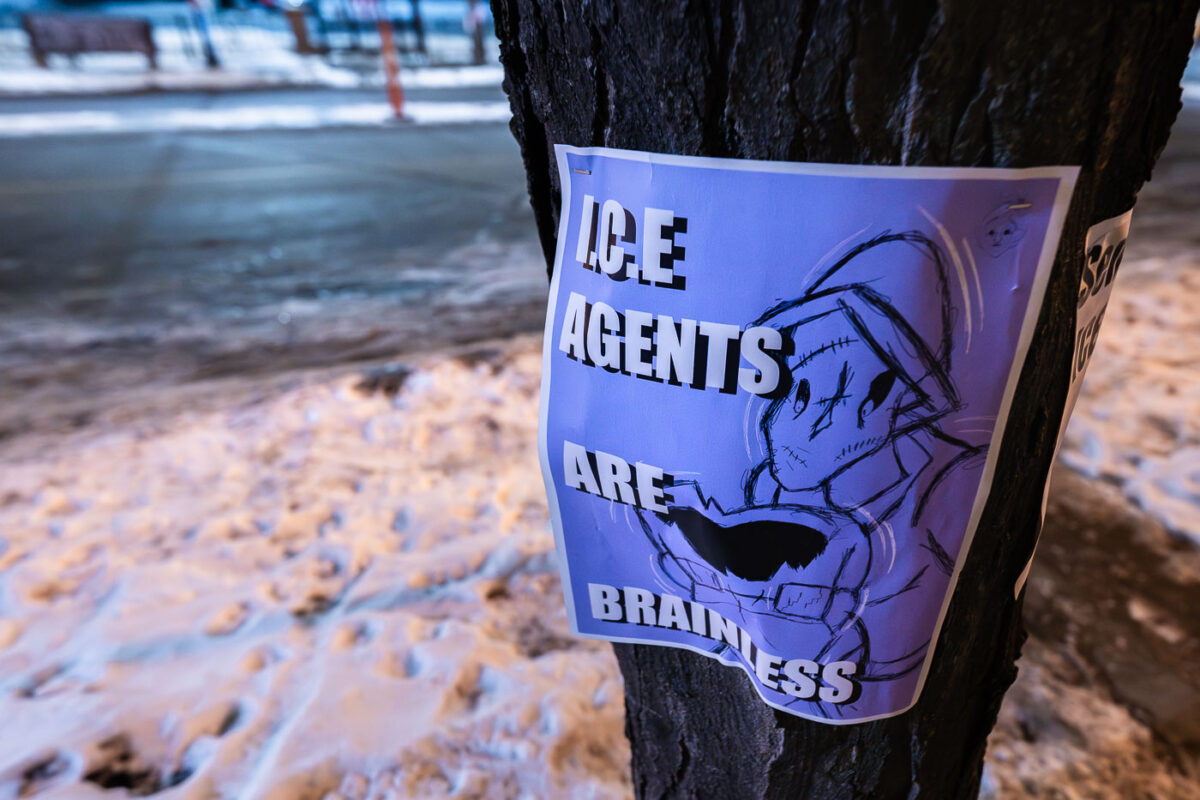 A flyer protesting ICE agents is posted on a tree in Minneapolis. The flyer reads "ICE AGENTS ARE BRAINLESS" and includes a crude drawing.