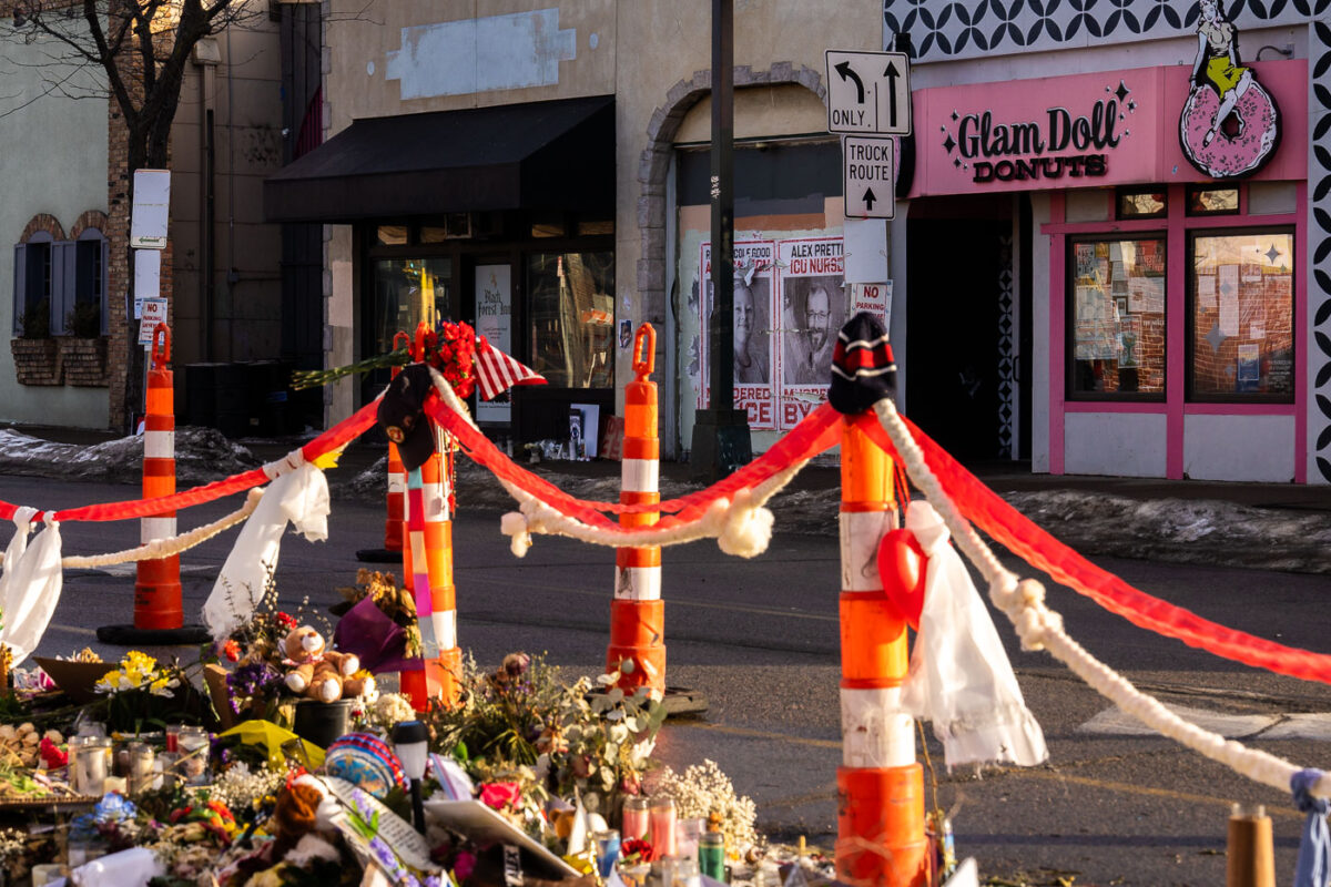 Posters hang across from the Alex Pretti Memorial and next to Glam Doll Donuts reading:
RENEE GOOD AMERICAN MOM MURDERED BY ICE
ALEX PRETTI ICU NURSE MURDERED BY ICE