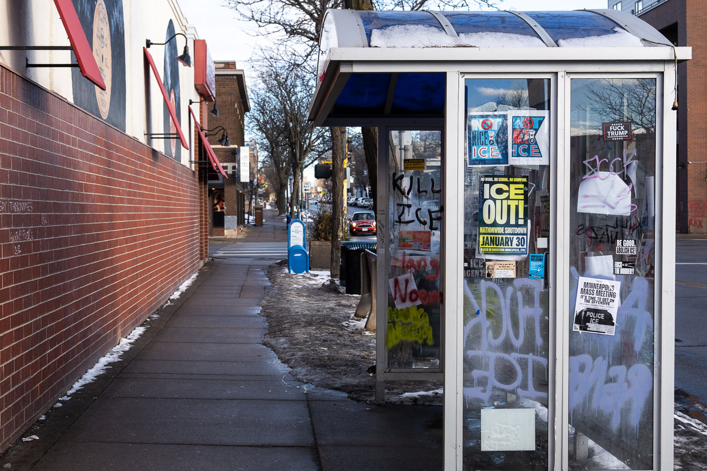 Minneapolis bus stop on Nicollet Avenue displays graffiti and protest posters against ICE and the Trump administration, referencing a January 30th shutdown.
