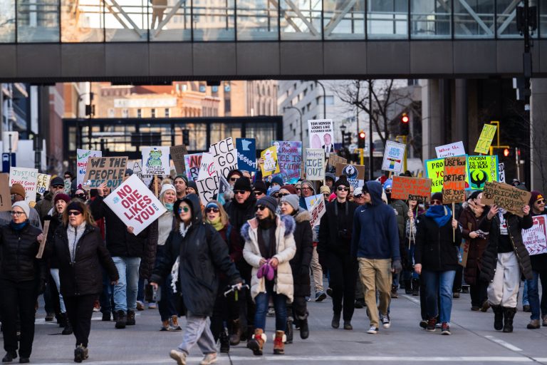 Minneapolis ICE Protest March Downtown 1 Protesters march downtown in Minneapolis holding signs against ICE.