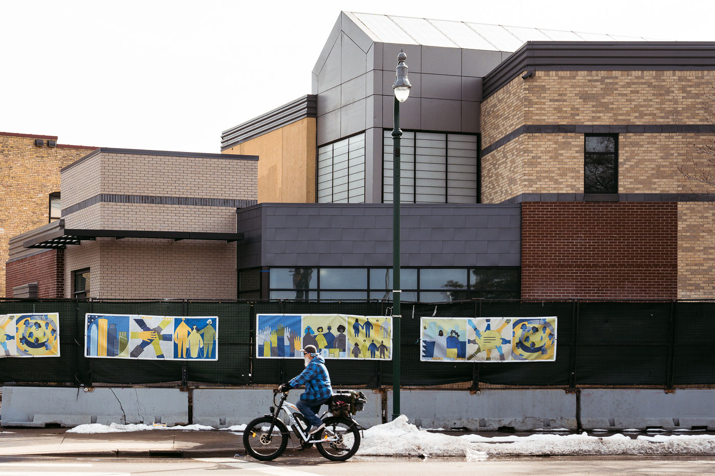 Construction on the former Minneapolis Police 3rd Precinct building vestibule, featuring community-themed banners on fencing.