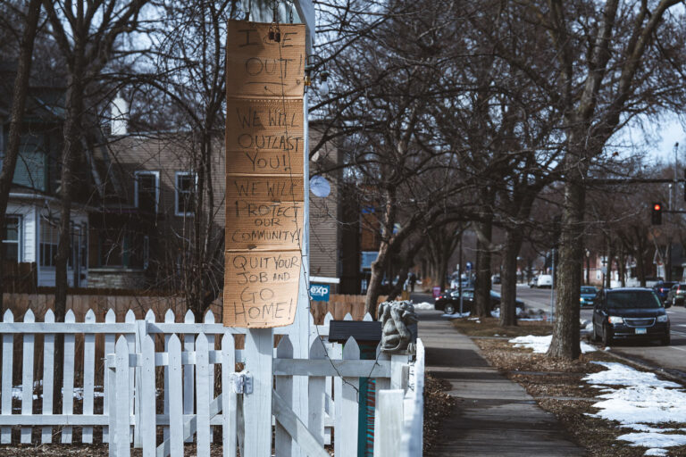 Minneapolis Protest Sign Against ICE 3 A handmade protest sign against ICE is displayed on a pole in Minneapolis, reading "ICE OUT! WE WILL OUTLAST YOU! WE WILL PROTECT OUR COMMUNITY! QUIT YOUR JOB AND GO HOME!"