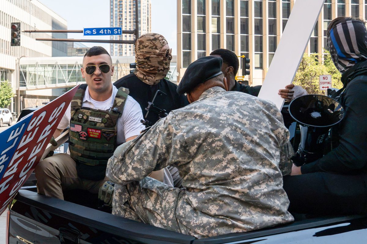 Men in military-style clothing and masks stand near a vehicle at South 4th Street in Minneapolis during a protest.