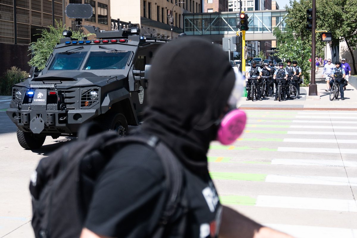Counter protester facing armored vehicle and police during Minneapolis white supremacist rally confrontation.
