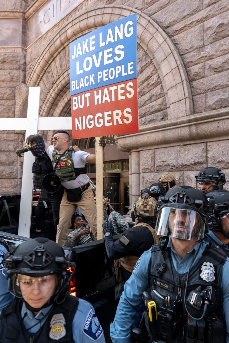 Counter protester holding sign criticizing Jake Lang at Minneapolis City Hall during white supremacist rally.