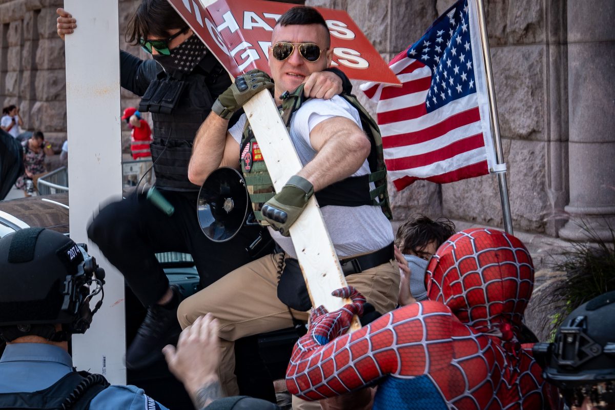 Armed counter-protester in Spider-Man costume confronts man in military gear during Jake Lang rally at Minneapolis City Hall.