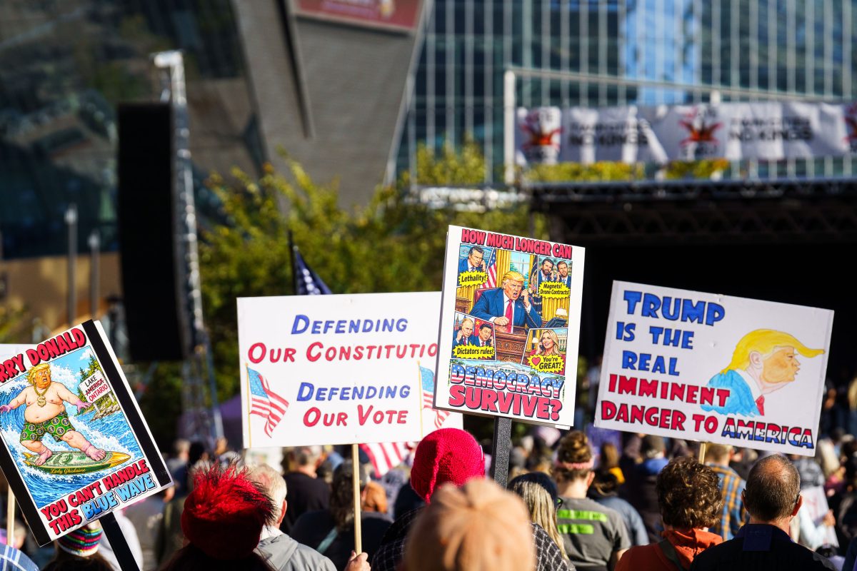 Protesters hold comic-style signs with political messages at a downtown Minneapolis rally.