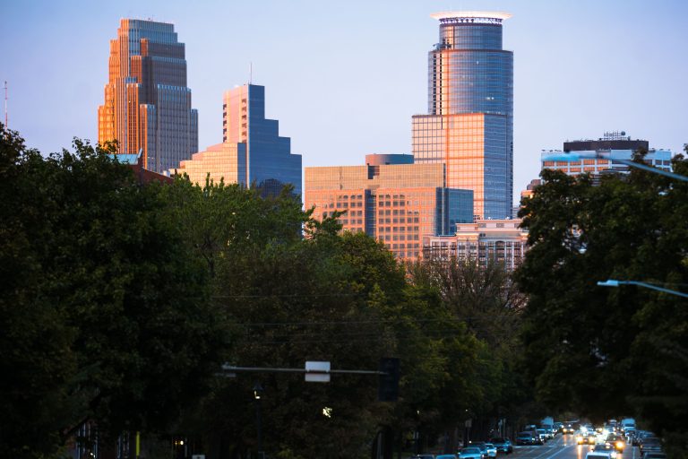 Downtown Minneapolis Skyline Seen from Portland Avenue 2 Minneapolis downtown skyline with Wells Fargo Center, Two22, and US Bank Plaza visible beyond trees along Portland Avenue.