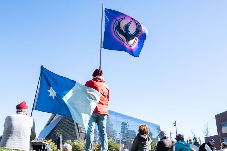 Flags Fly at the "No Kings" Rally Near U.S. Bank Stadium 4 Protesters holding flags at the NO KINGS rally in Minneapolis Commons Park beneath clear skies.