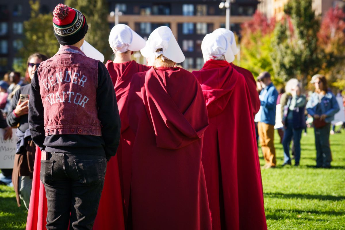People in red robes and white bonnets stand at a Minneapolis protest rally against authoritarian governance.