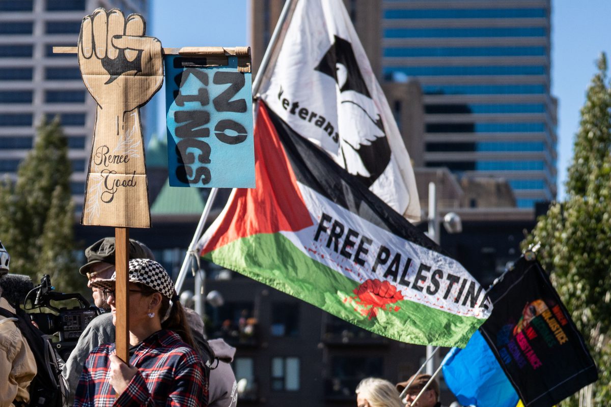 Protesters at Commons Park in Minneapolis display signs including a raised fist and "Free Palestine" flag during the No Kings rally.