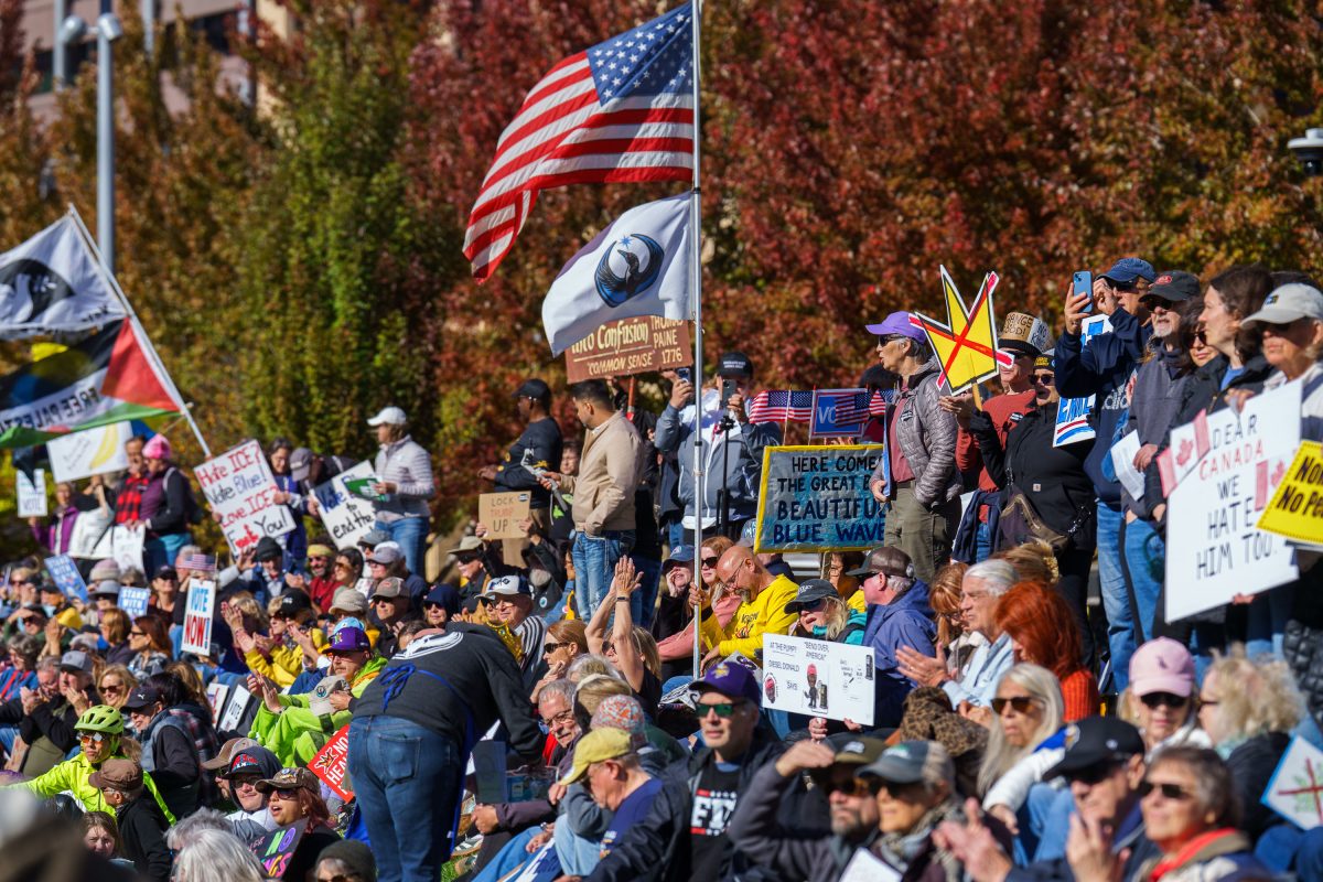 A crowd gathers at the Minneapolis NO KINGS rally, holding signs and American flags during a public demonstration.