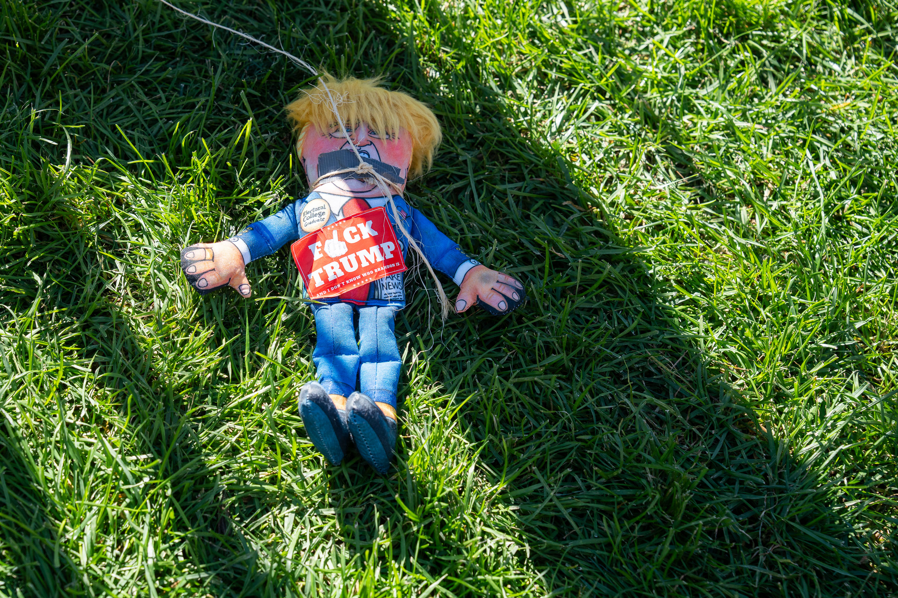 Action figure wearing "Trump" clothing lies on grass at the NO KINGS rally in Minneapolis.