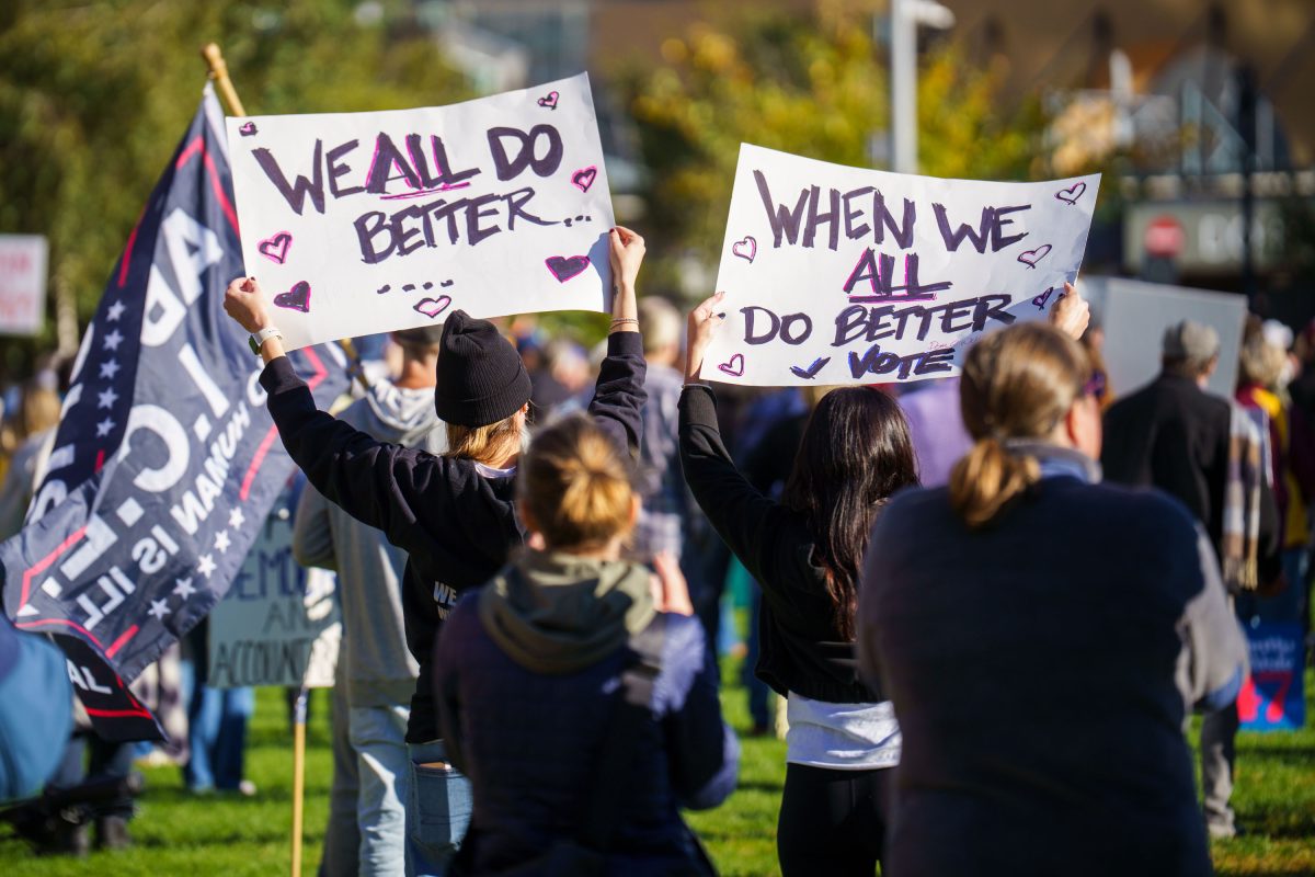 Protesters hold handmade signs reading "We all do better" and "When we all do better vote" at a Minneapolis rally.