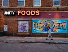 A man walks in front of the George Floyd mural on the side of "Unity Foods". Unity Foods was formerly named Cup Foods.