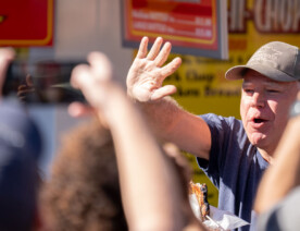 Tim Walz waves to those gathered outside the dairy building after biting into his Pork Chop On A Stick at the Minnesota State Fair on September 1, 2024.
