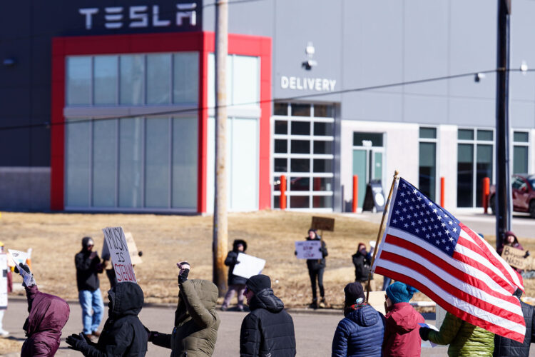 Protester with an American flag outside a Tesla facility just outside of Minneapolis. Protester with an American flag outside a Tesla facility just outside of Minneapolis.