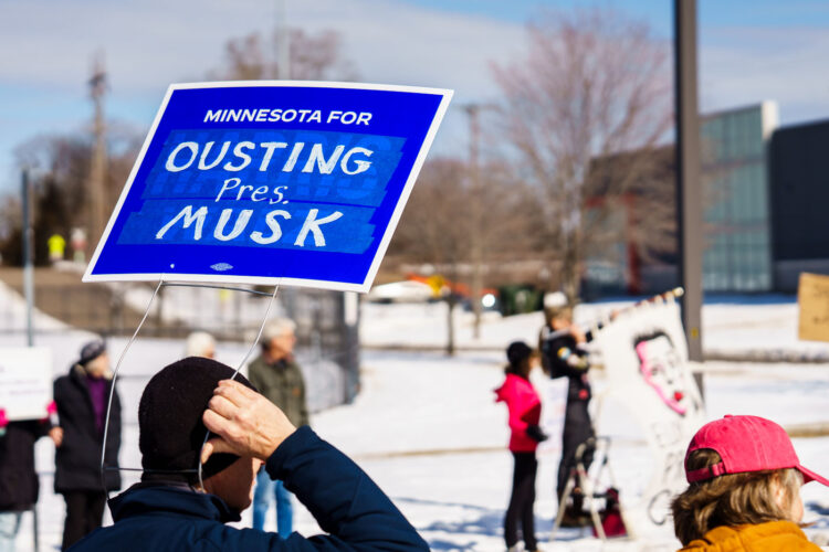 Protester with a sign reading "Minnesota for Ousting Pres. Musk" at a Tesla Facility just outside of Minneapolis (Golden Valley) on March 8, 2025.This is the 4th week in a row protesters have gathered here as part of the nationwide Tesla Takedown organizing. Protester with a sign reading "Minnesota for Ousting Pres. Musk" at a Tesla Facility just outside of Minneapolis (Golden Valley) on March 8, 2025.This is the 4th week in a row protesters have gathered here as part of the nationwide Tesla Takedown organizing.